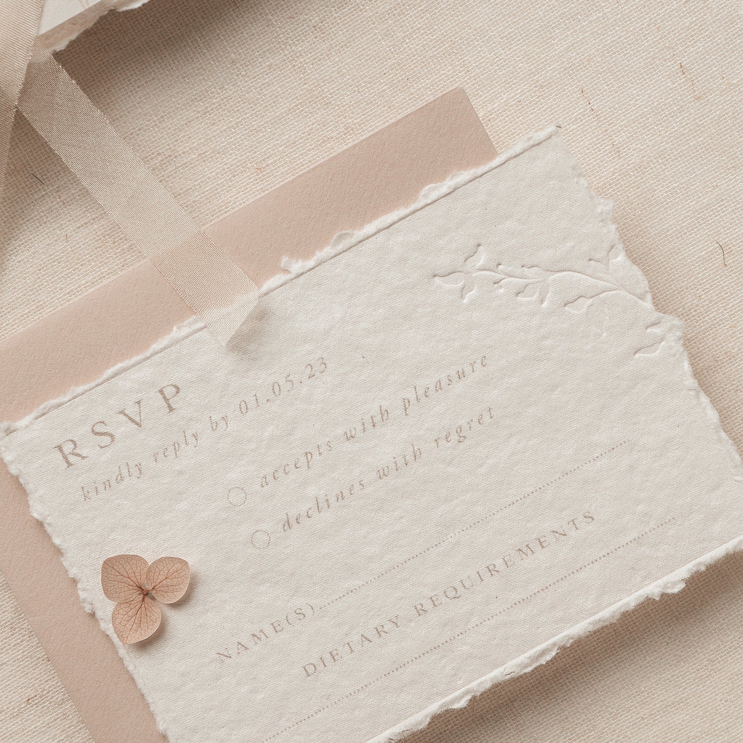 wedding rsvp card with blind letterpress leaf vine printed on handmade cotton paper and styled with a light blush return envelope 