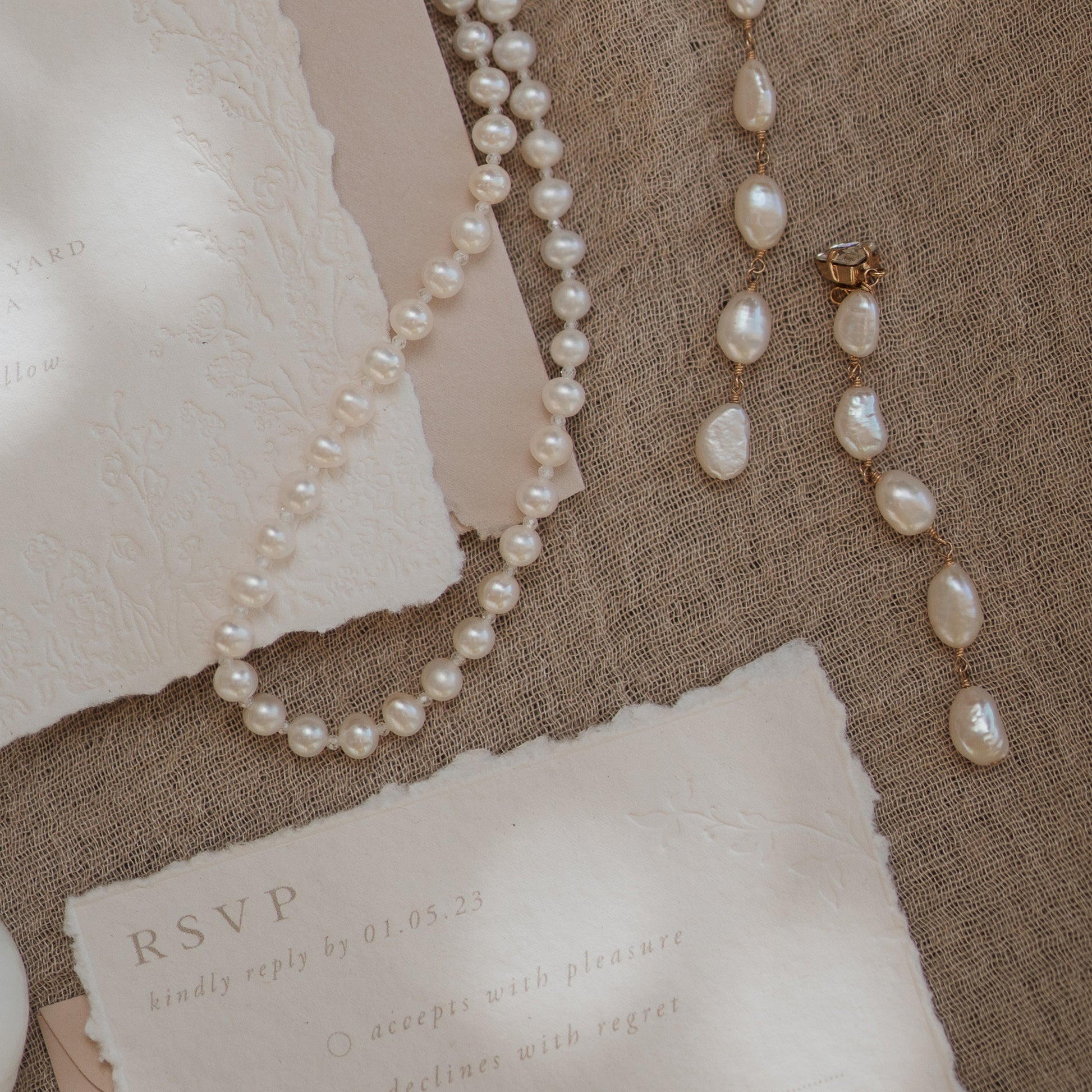 wedding rsvp card with blind letterpress leaf vine printed on handmade cotton paper and styled with a light blush return envelope and pearl jewellery 