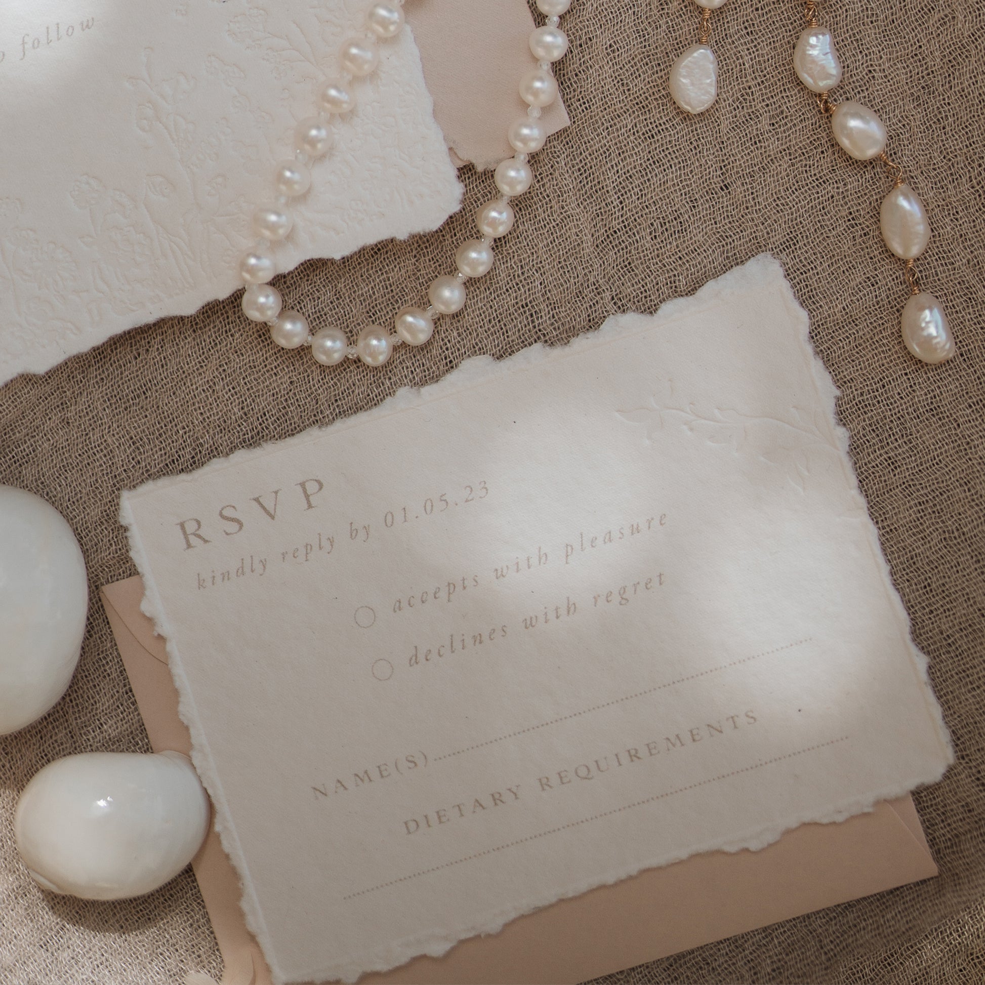 wedding rsvp card with blind letterpress leaf vine printed on handmade cotton paper and styled with a light blush return envelope 