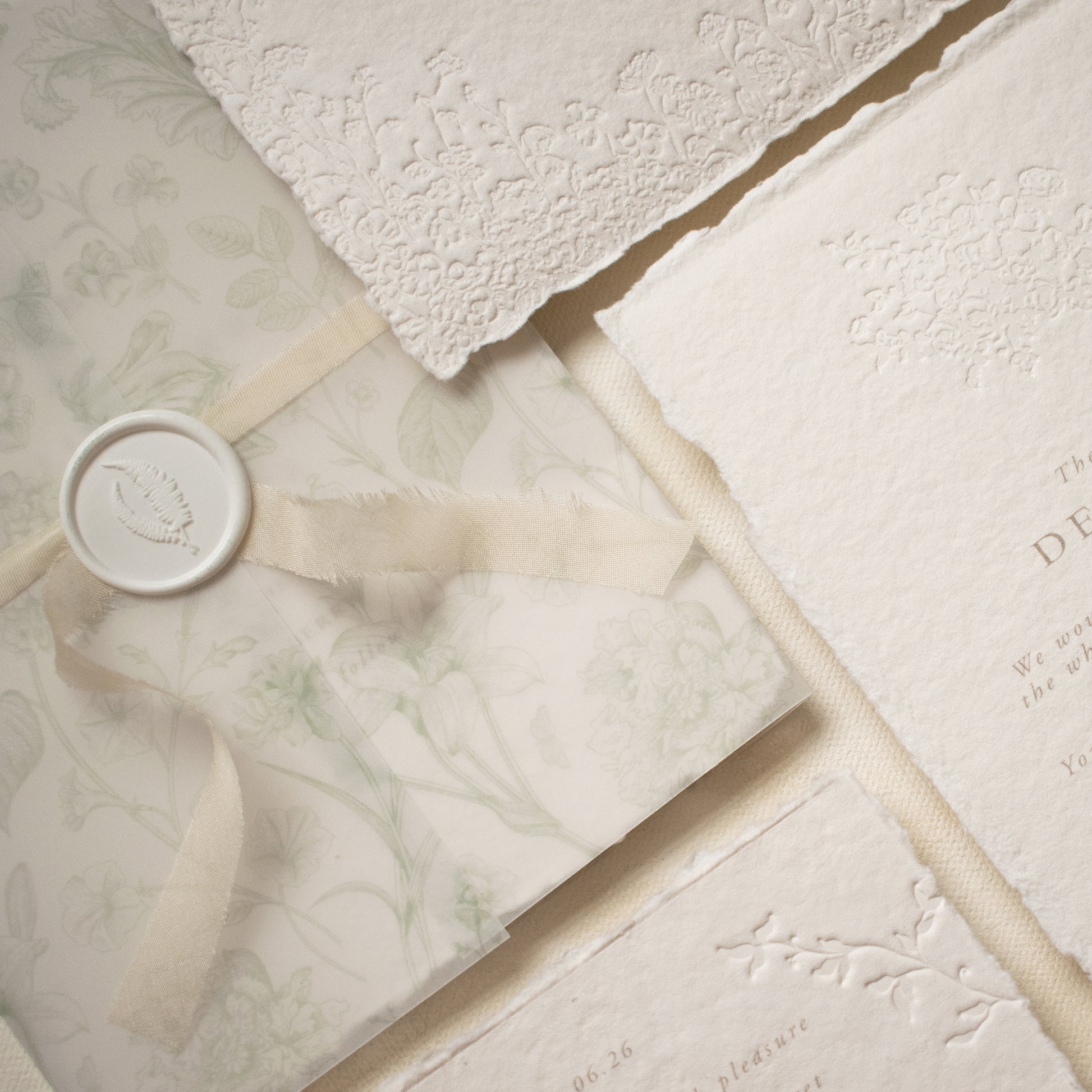 a close up of a sage green floral vellum wrap with letterpress wedding invitation suite on ivory handmade cotton paper
